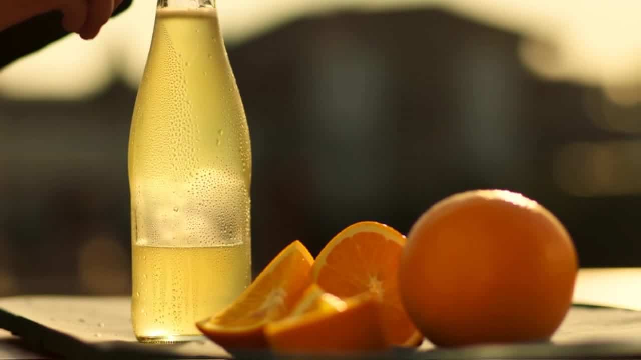Luma Ray 2 AI video example: **Scene (plain language):** A glass bottle of sparkling citrus drink sits on a sunlit outdoor café table in...